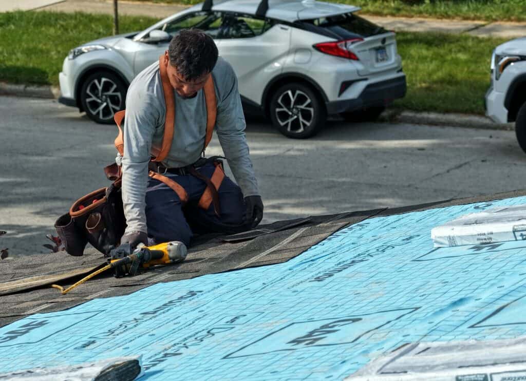 Proliance roofer in a safety harness installing new shingles over underlayment